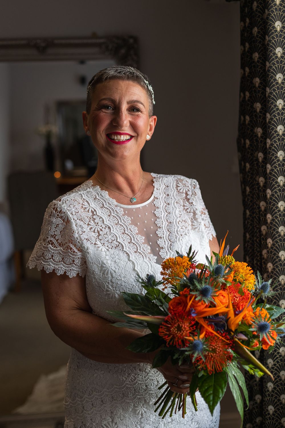 Wedding bouquet with vibrant orange and blue tropical flowers against white lace.