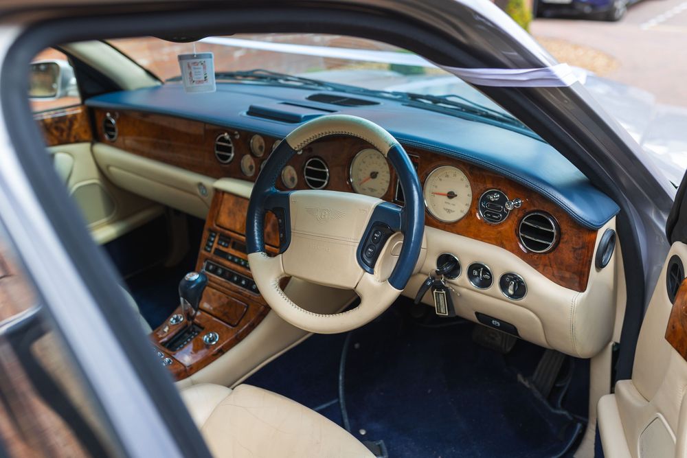 Luxury car interior dashboard showing wood trim details, beige leather, and classic analog instrument cluster.