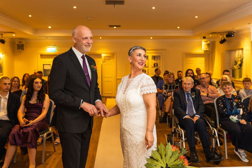 Wedding ceremony guests gathered in an elegant yellow-lit reception hall with recessed lighting.