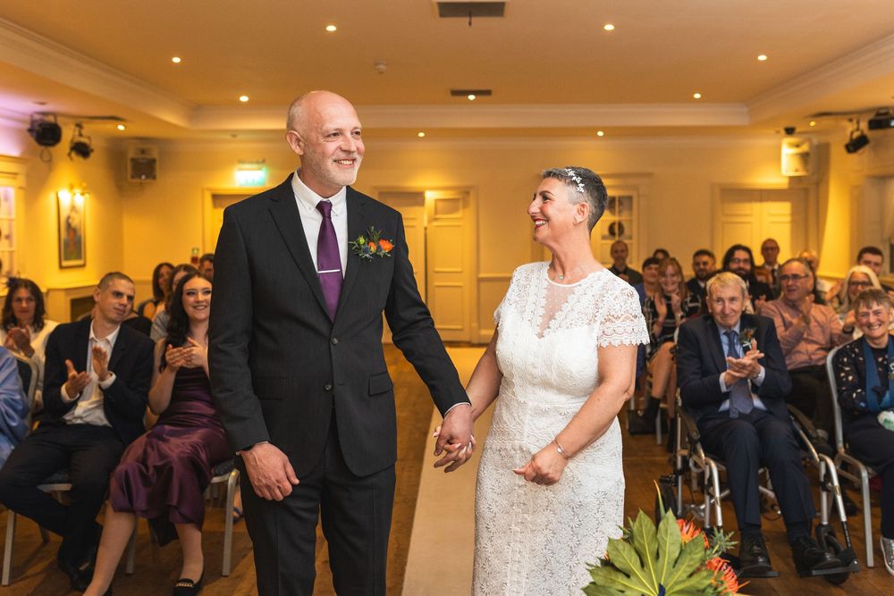 A large wedding reception room with guests mingling under warm lighting and decorative ceiling fixtures.
