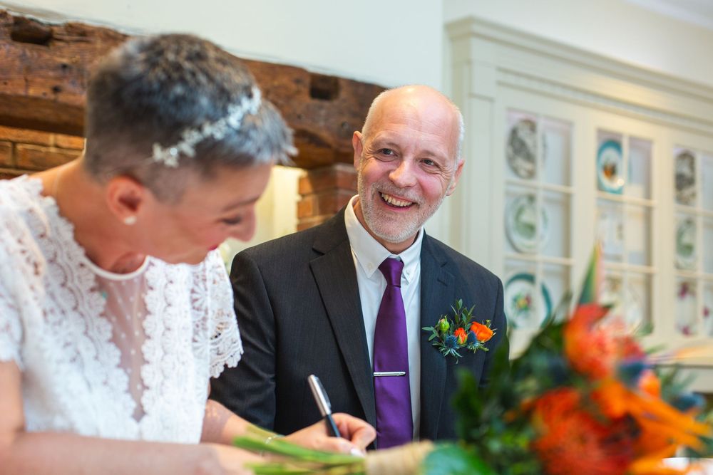 People signing documents at a formal event with bright orange and red floral decorations on the table.