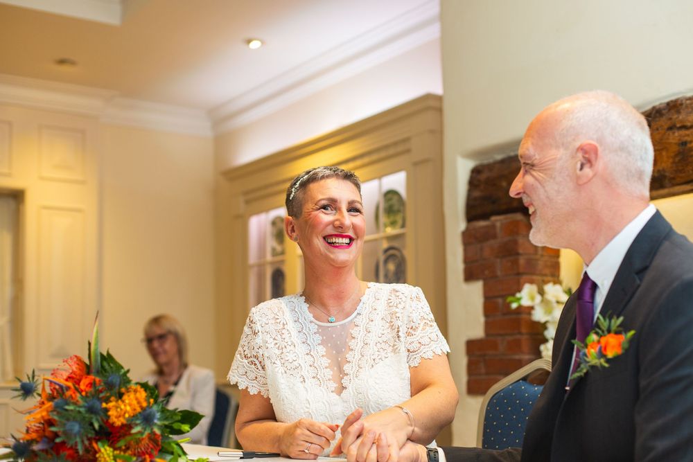 Wedding reception guests seated at tables with orange floral centerpieces share laughter during a celebration.
