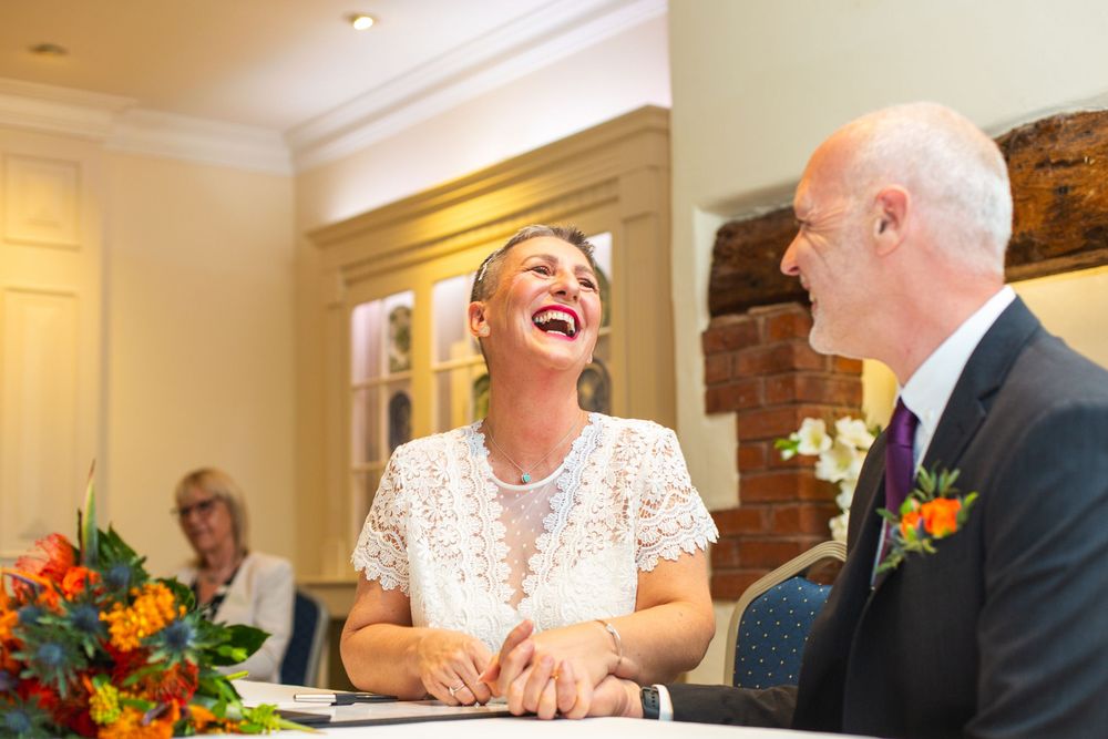 Wedding guests share joyful laughter during an elegant indoor reception with warm lighting and floral decorations.