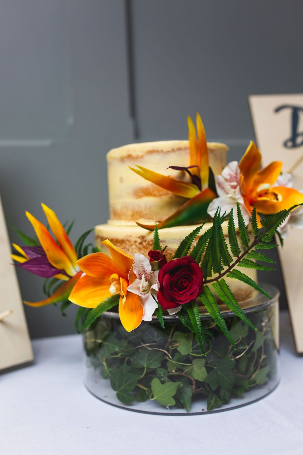 Tropical floral centerpiece with orange birds of paradise and red roses arranged in a clear glass bowl.