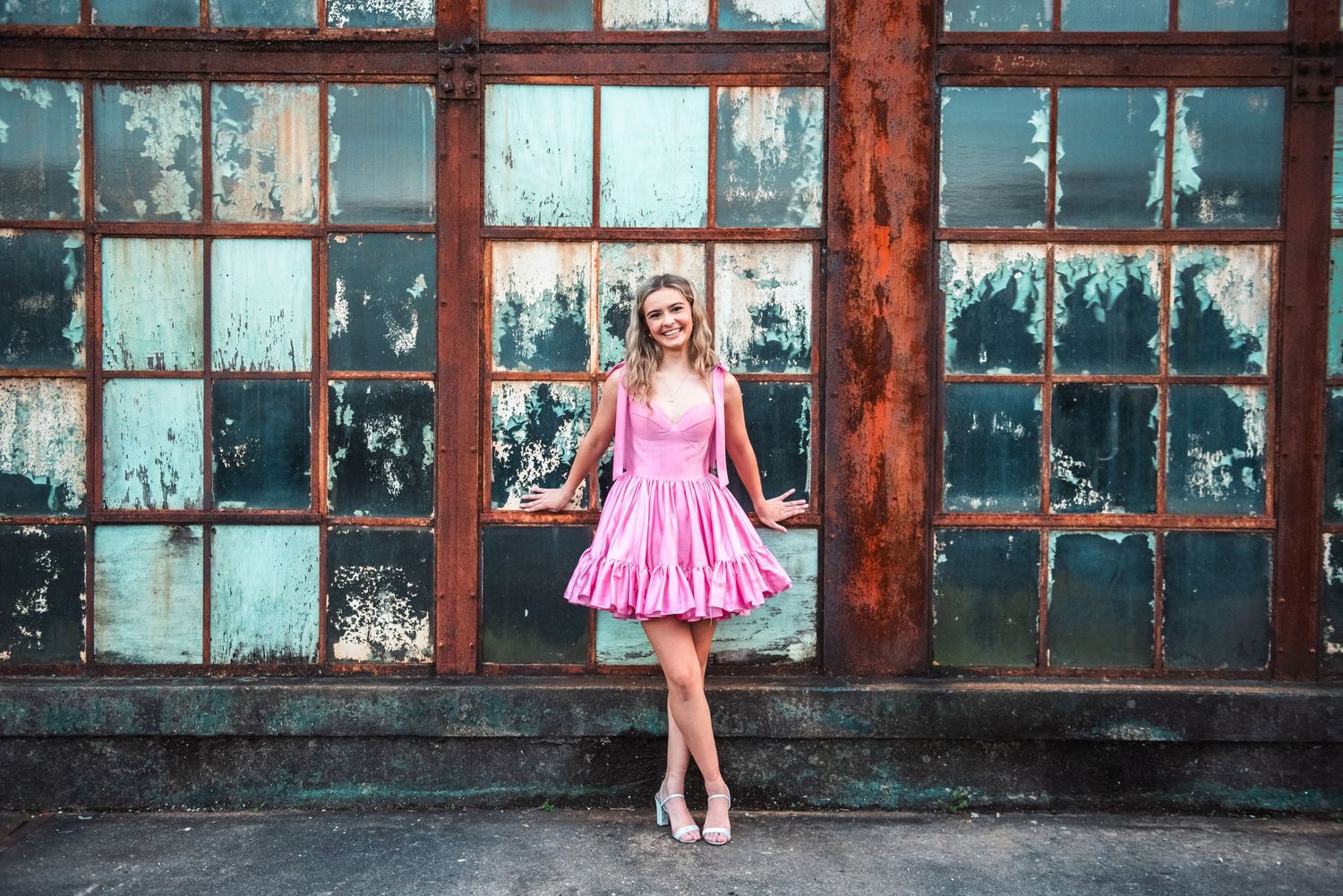 A ballet dancer in a bright pink tutu performs graceful movements in front of an industrial window backdrop.