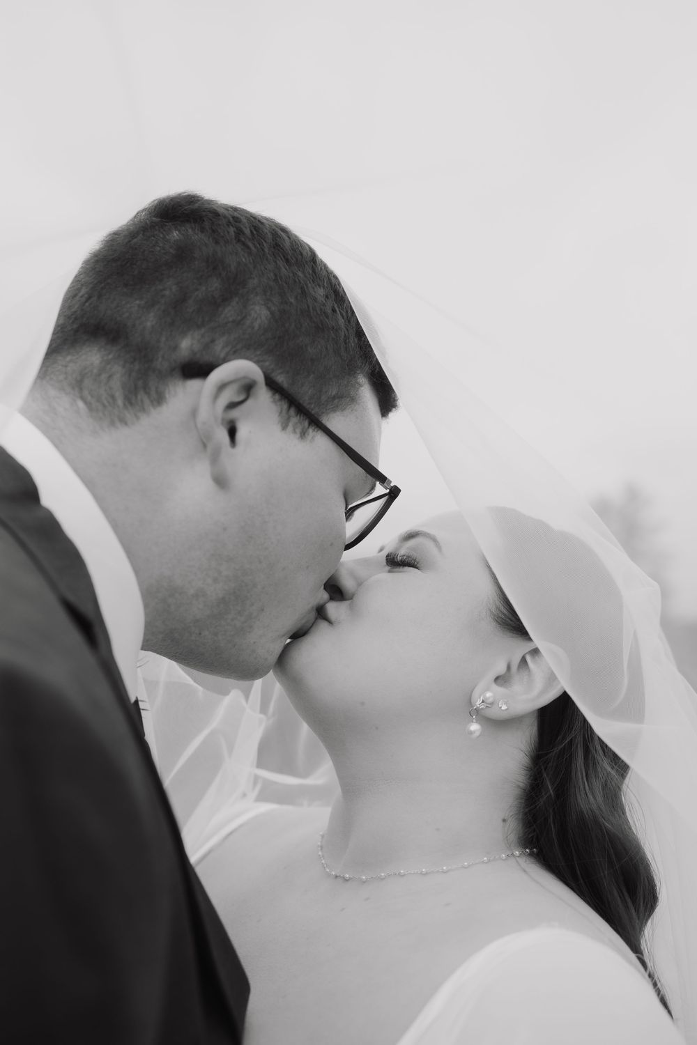 A romantic black and white wedding photo sequence showing a couple sharing a tender kiss under a flowing white veil.