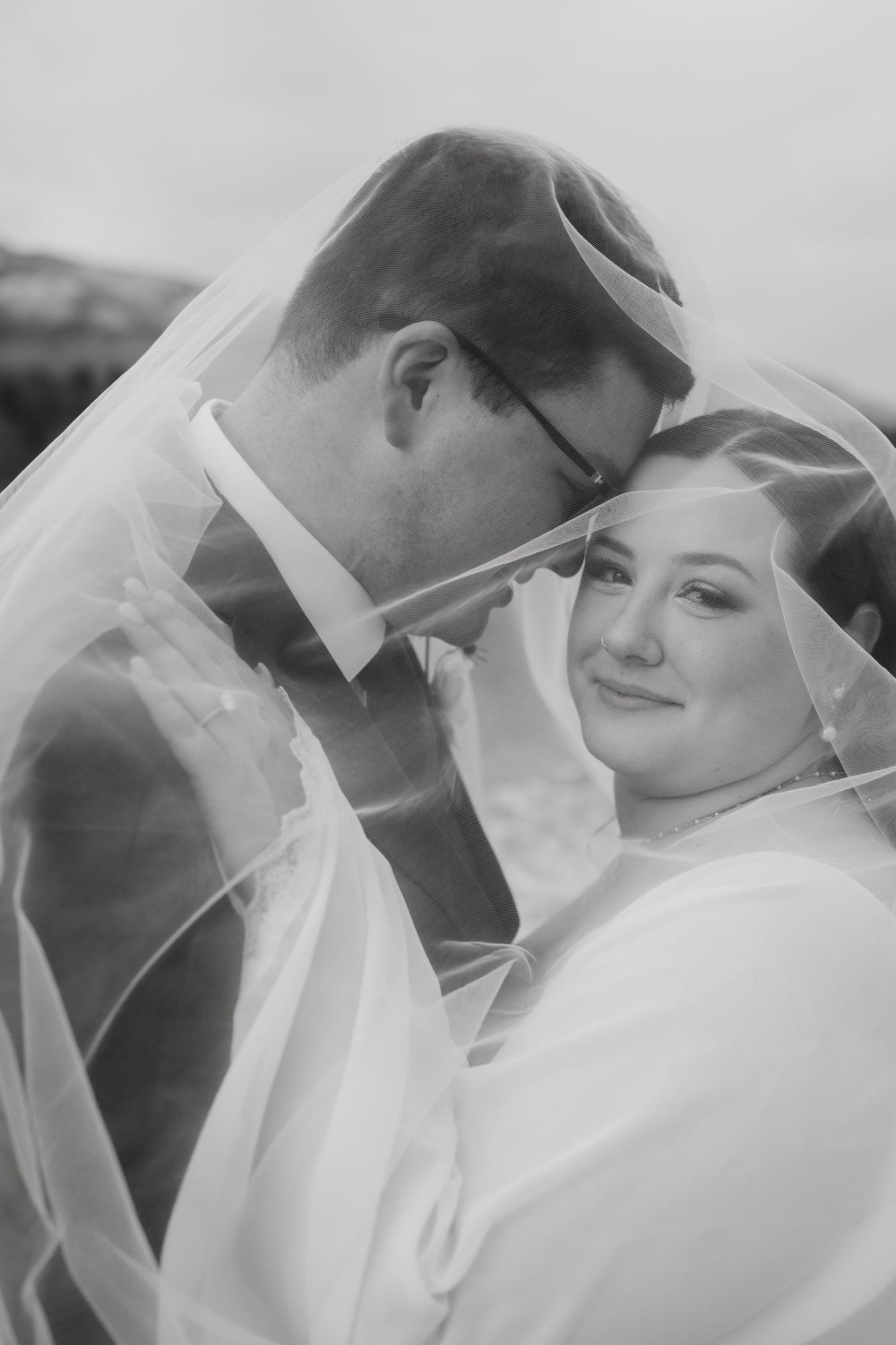 A romantic black and white wedding portrait showing a tender moment between newlyweds under a delicate veil.