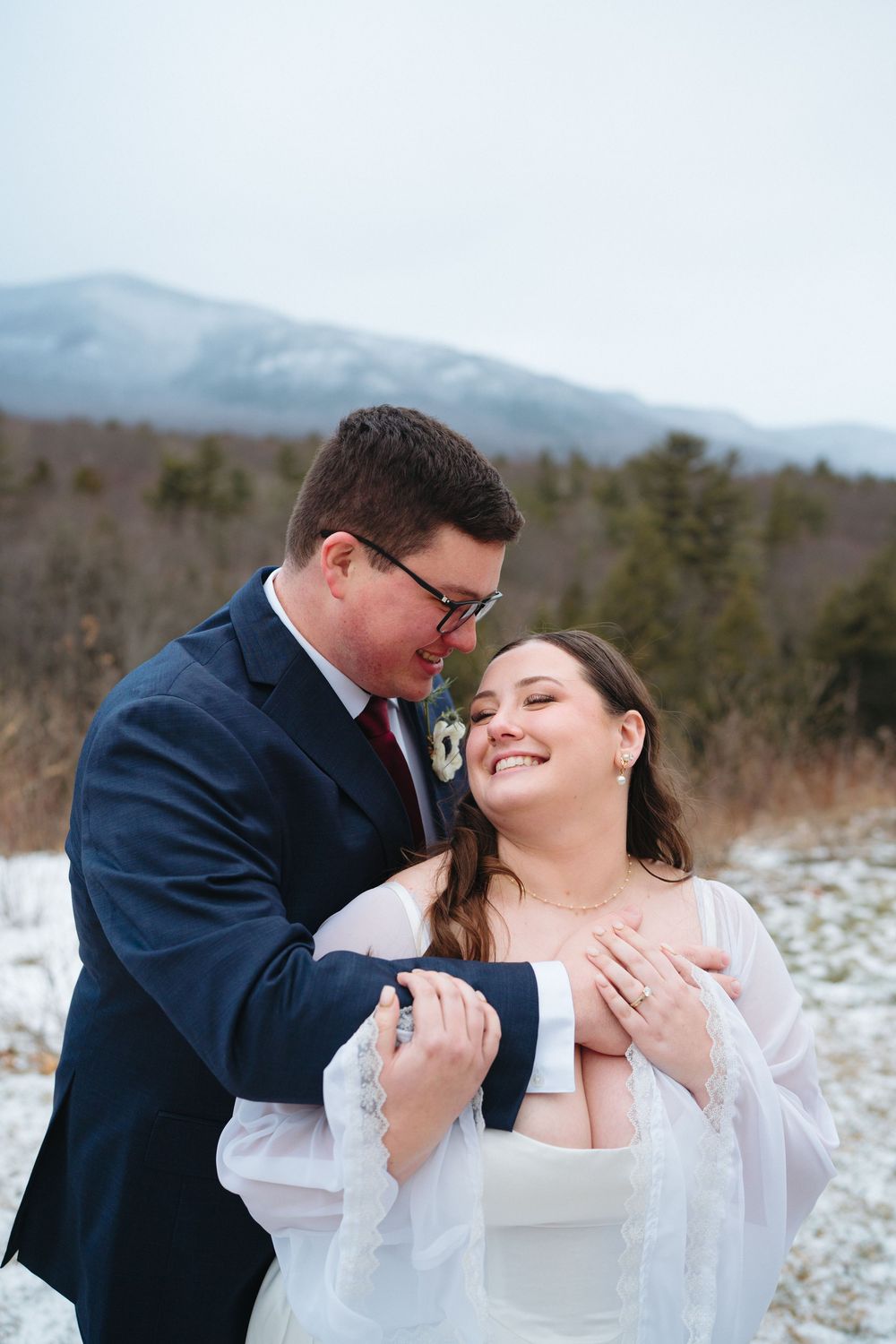 A romantic winter wedding moment captured against snowy mountains with the couple embracing.