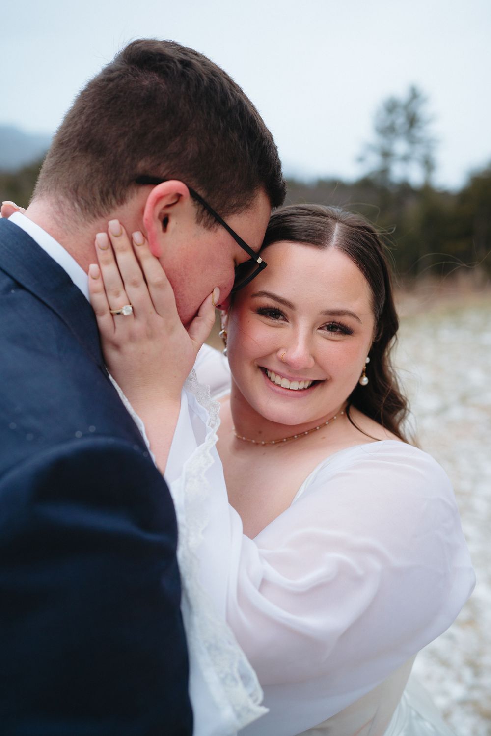 Romantic wedding couple embraces in a snowy winter field wearing formal attire and sharing intimate moments.