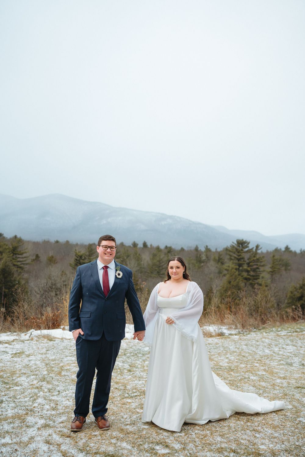A winter wedding portrait with snow-capped mountains and evergreen trees in the background.