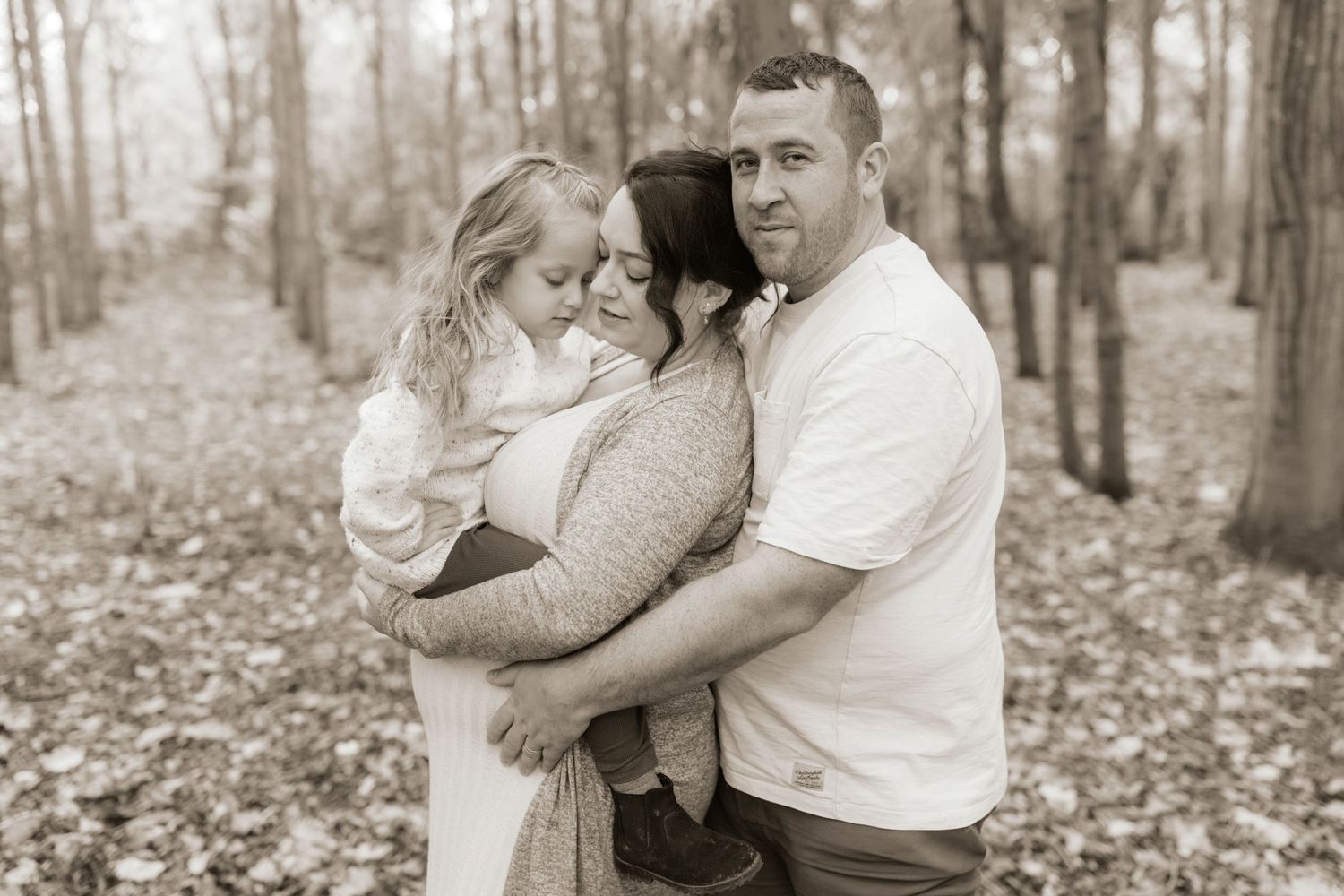 A series of romantic black and white photos showing a couple embracing in a forest setting during autumn.