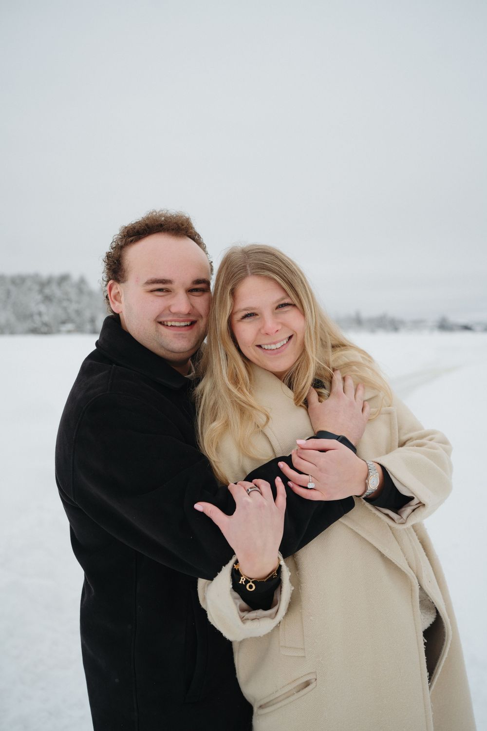 A happy couple embracing in the snow after getting engaged.