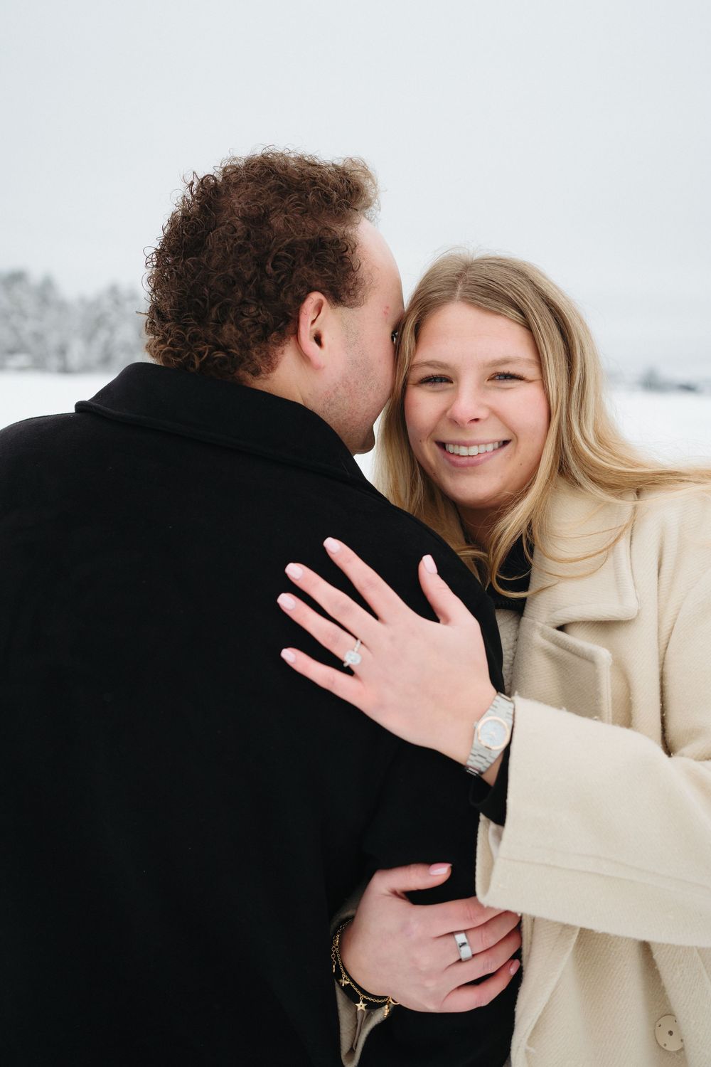 A couple sharing an intimate moment in the snow while showing off an engagement ring.