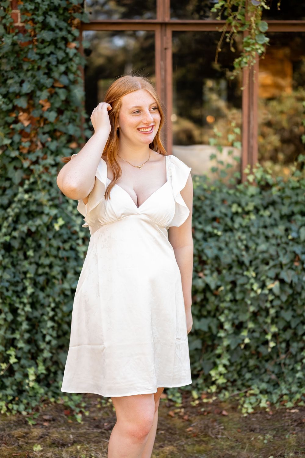 A breezy white dress is modeled in front of an ivy-covered wall with windows.