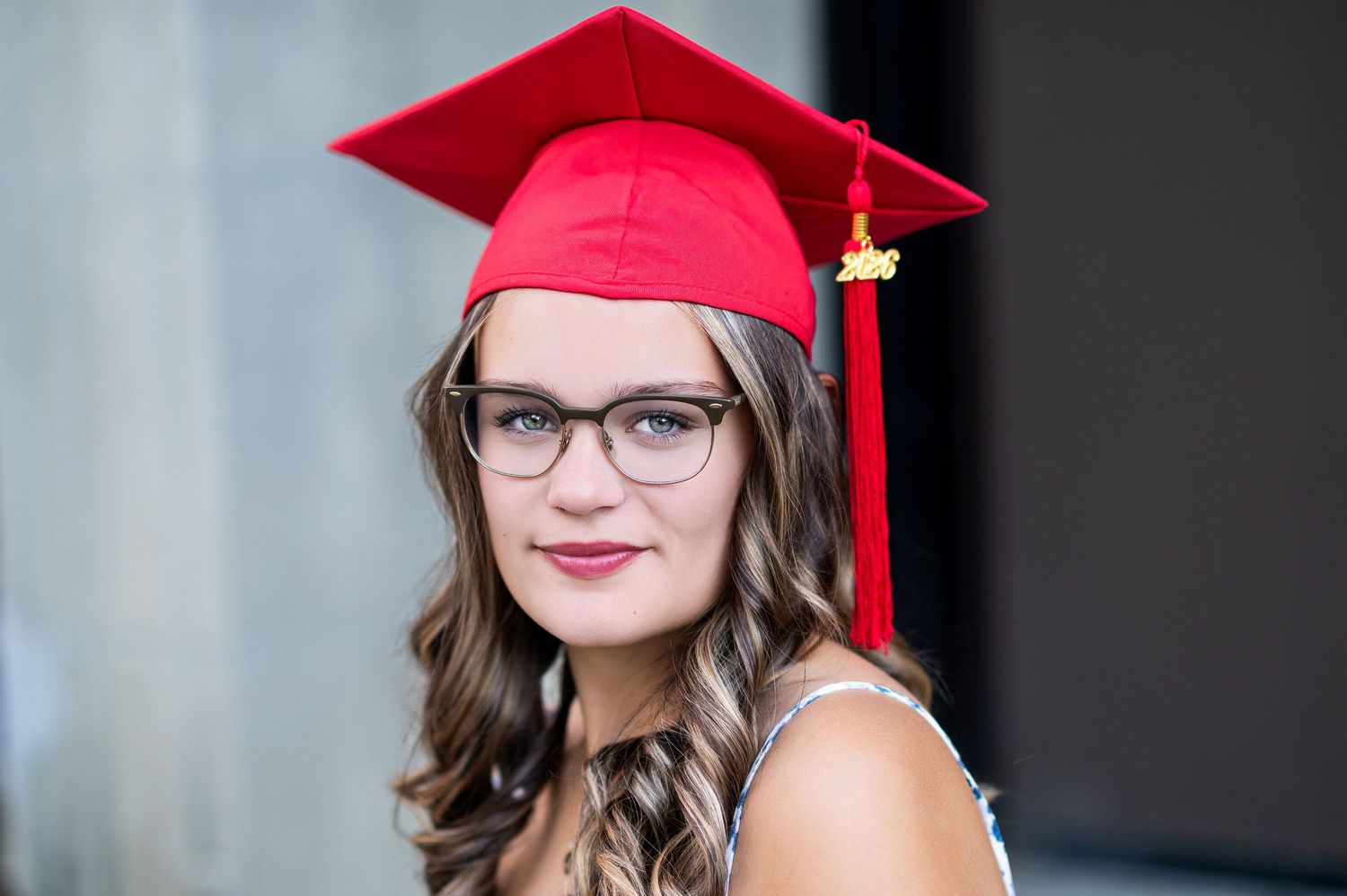 Graduate in red cap and gown posing for portraits against gray background.