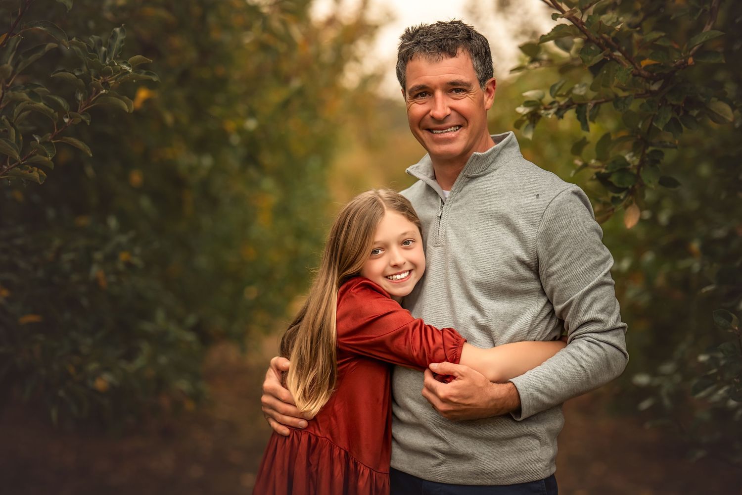 A parent and child share a tender moment while walking through an autumn orchard at sunset.