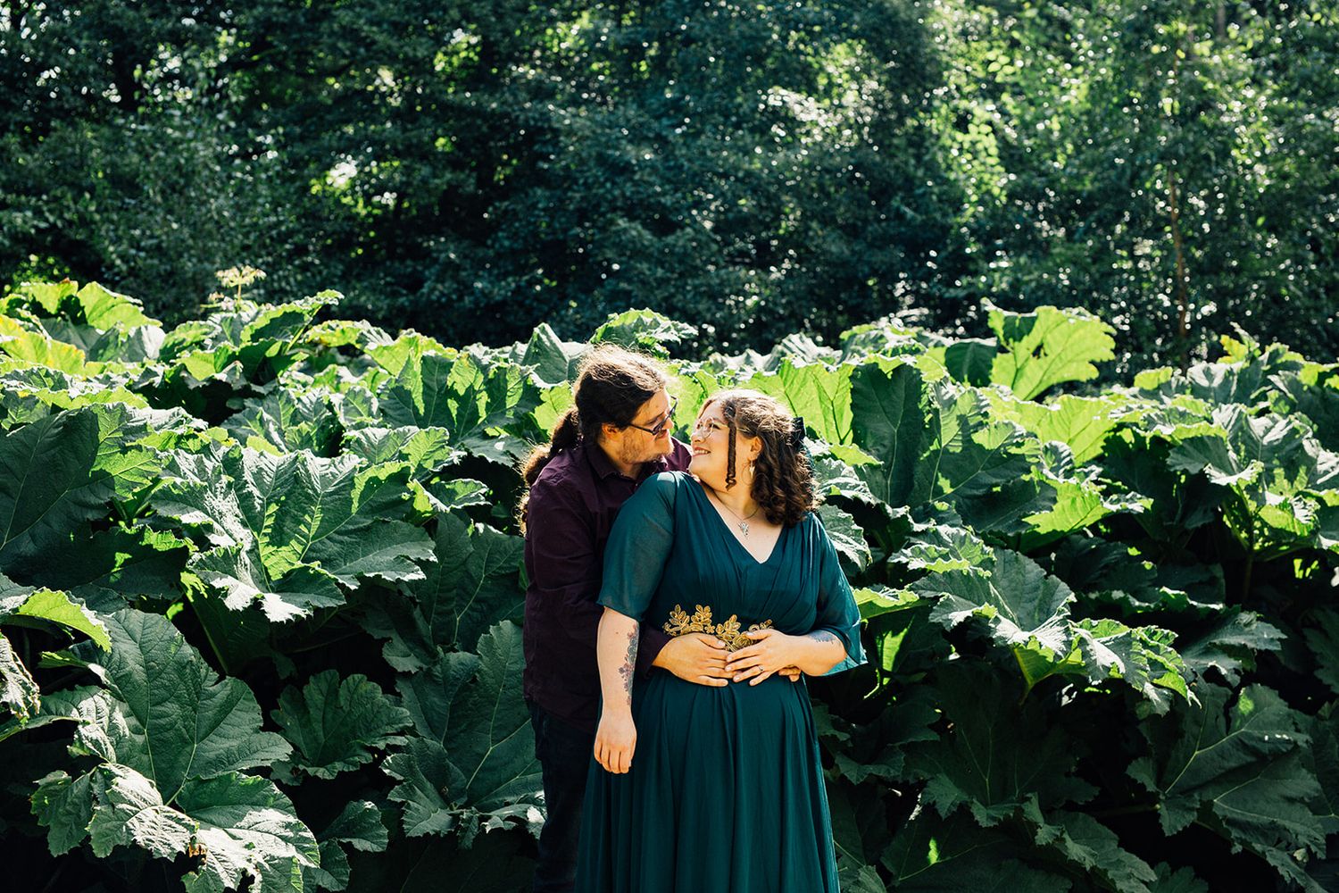 A person in a dark green dress picks fresh figs from a tree in a lush garden setting.