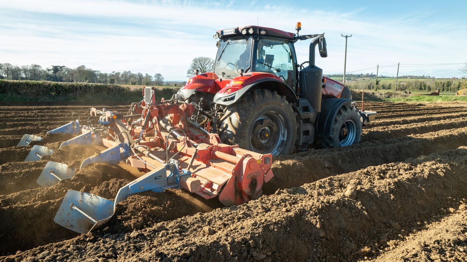 Red tractor pulling agricultural machinery through freshly tilled soil.