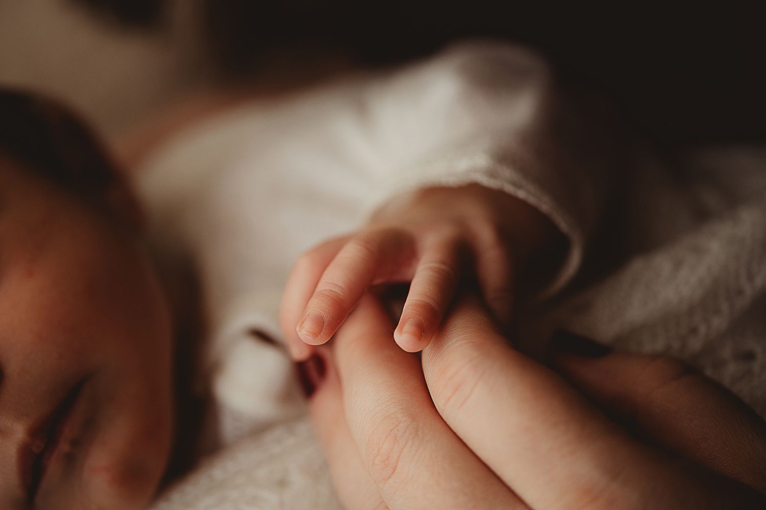 A newborn baby lying on white bedding while yawning and stretching their tiny arms.