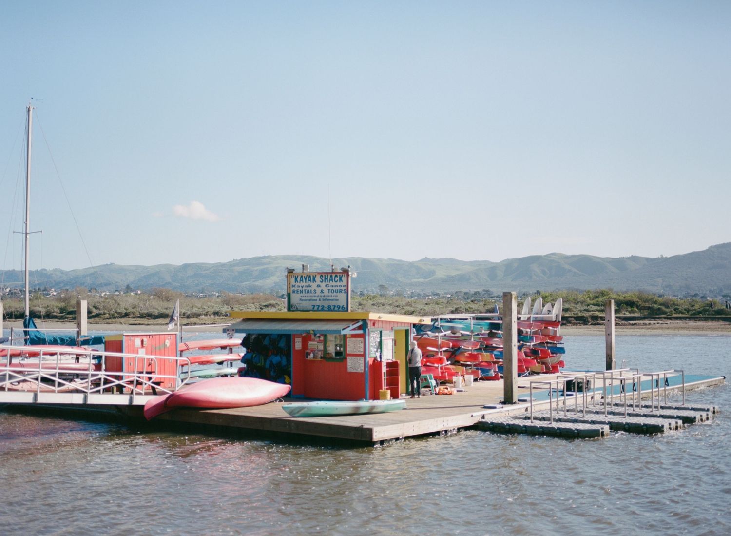 Panoramic view of a floating dock and boat marina with mountains in the background on a sunny day.
