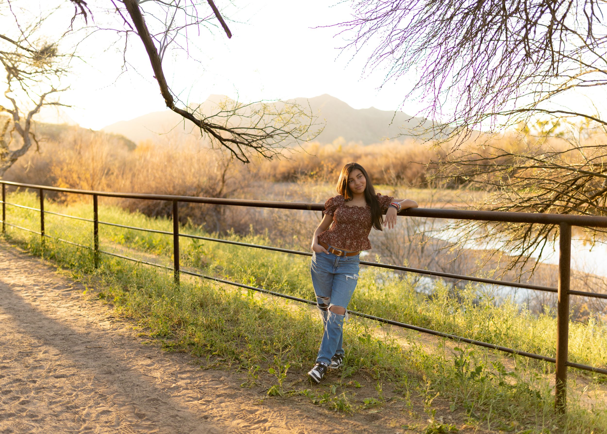 A person walks along a dirt path beside a wooden fence during sunset in a scenic rural landscape.