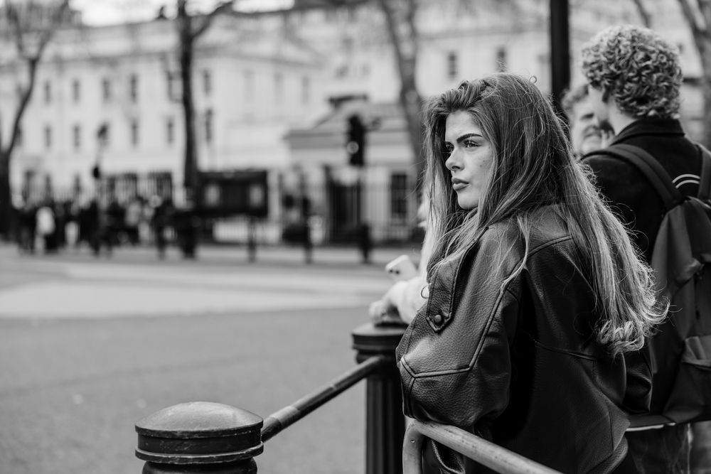 A black and white street photo of a glamorous young woman watching Changing of the Guard at Buckingham Palace