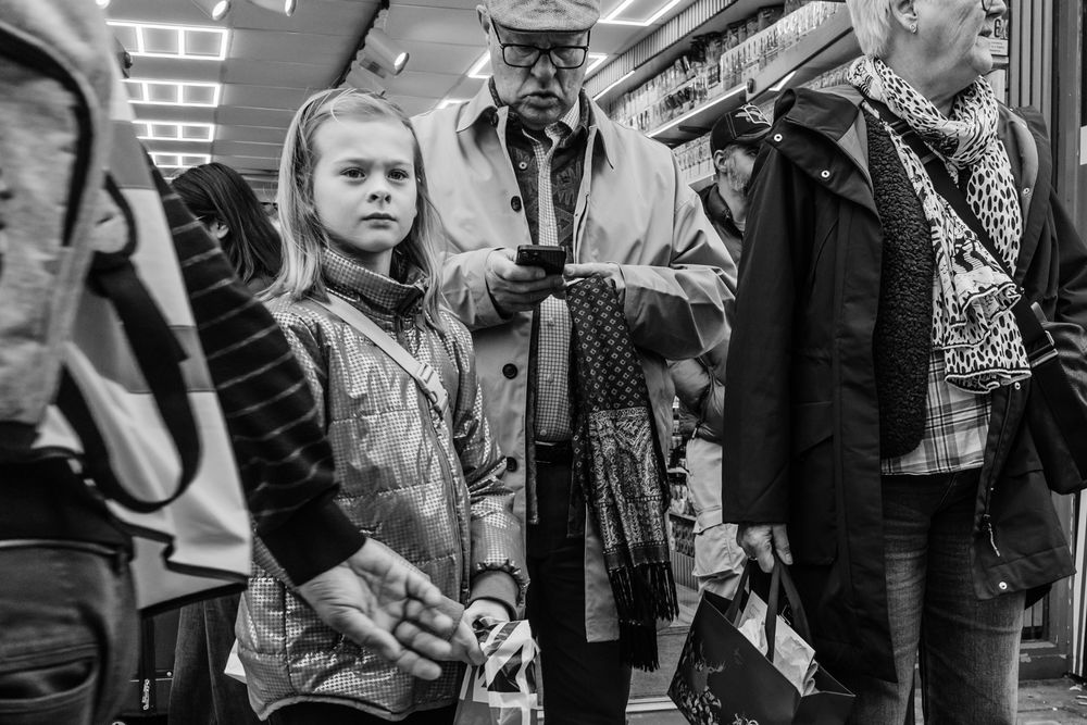 A black and white photograph shows a young girl looking seriously off into the distance as her grandfather checks his phone