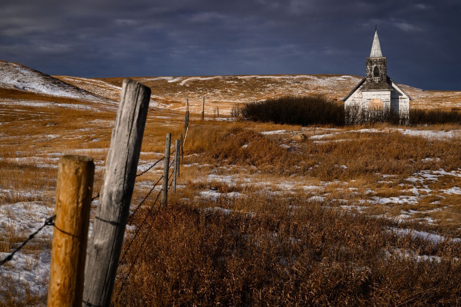 A panoramic winter landscape of a snow-covered prairie with a small white church visible in the distance.