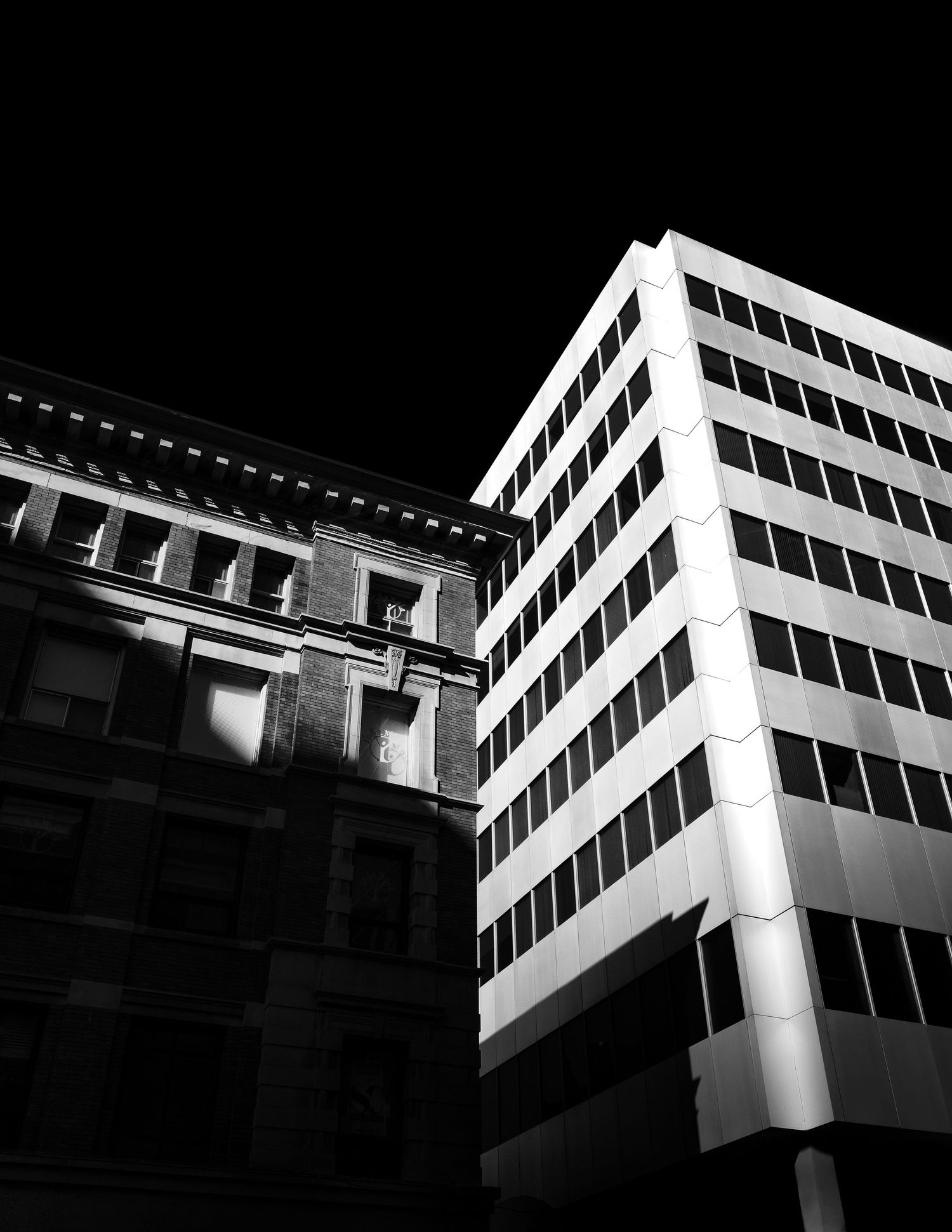 Black and white architectural photograph showing contrast between modern office tower and historic brick building.