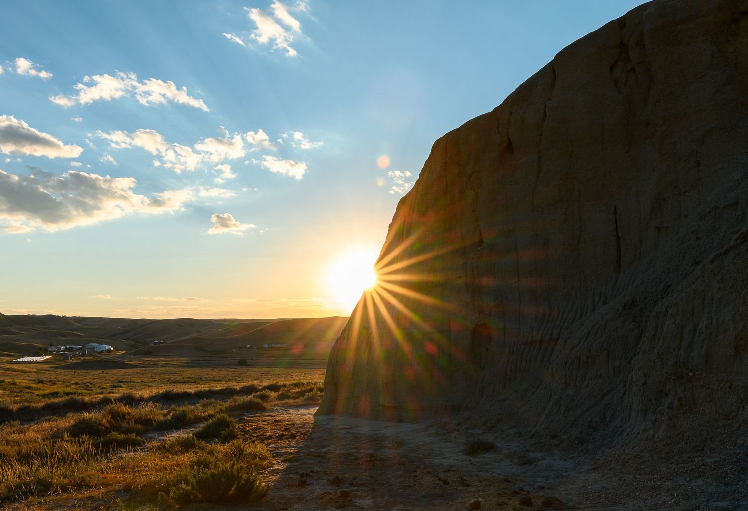 Dramatic sunset rays burst through clouds over rugged desert landscape with golden light illuminating rocky terrain.