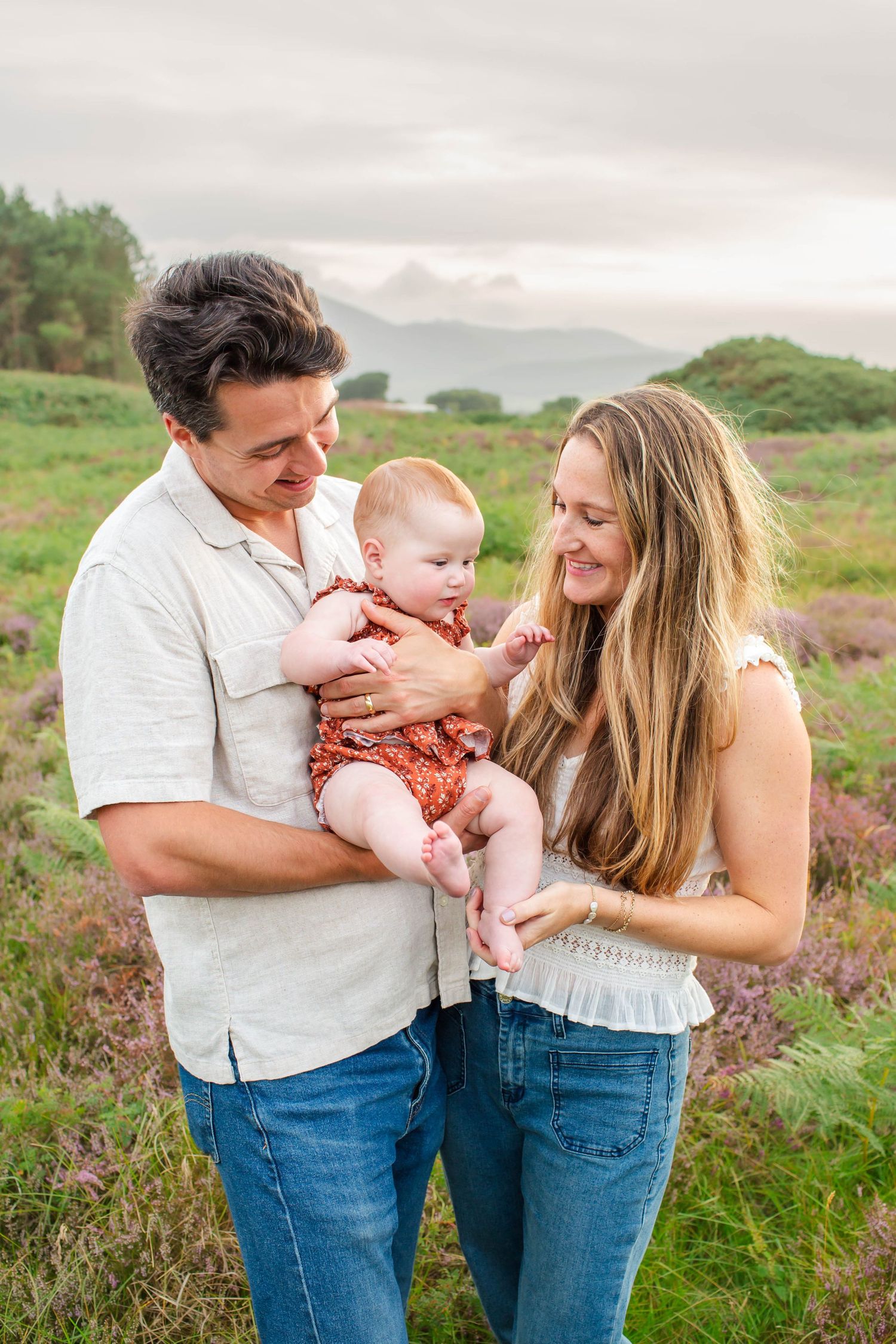A family shares tender moments together while standing in a blooming meadow at sunset.