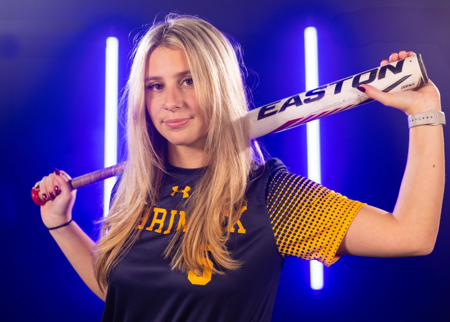 Athlete holds softball bat while wearing black and yellow uniform for sports photography session.