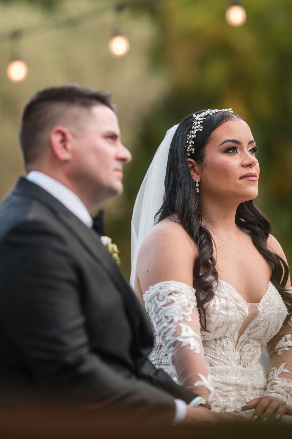 Bride and groom seated during an outdoor wedding ceremony surrounded by soft greenery and natural light