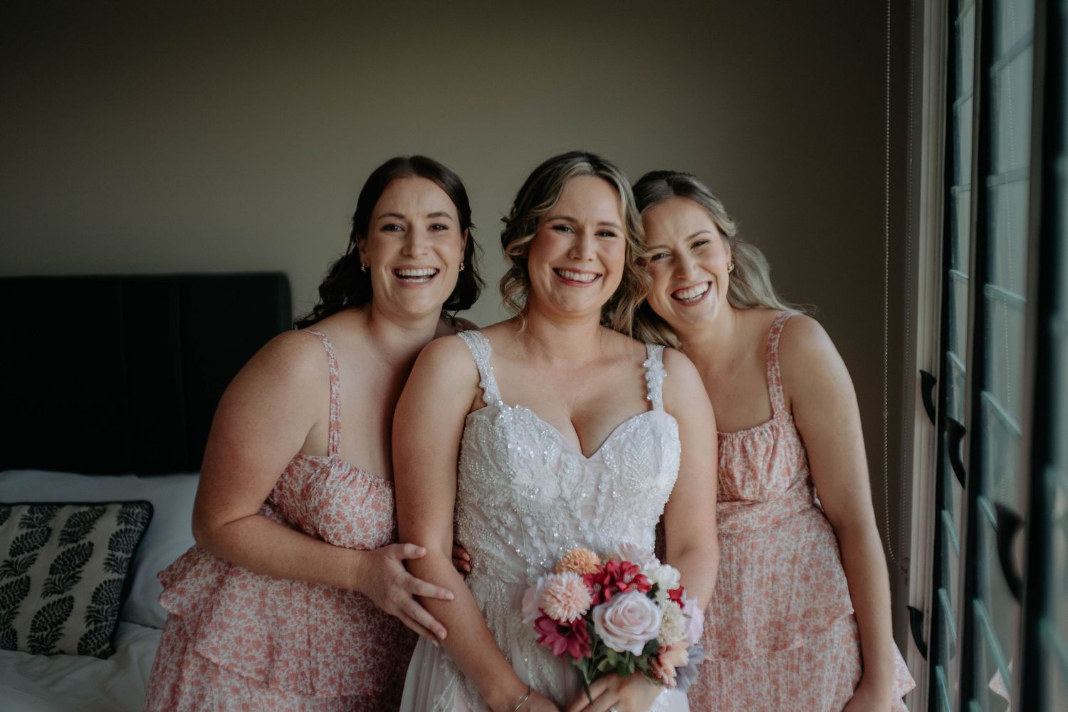A group of bridesmaids in pink and white dresses pose together while holding bouquets at a wedding.