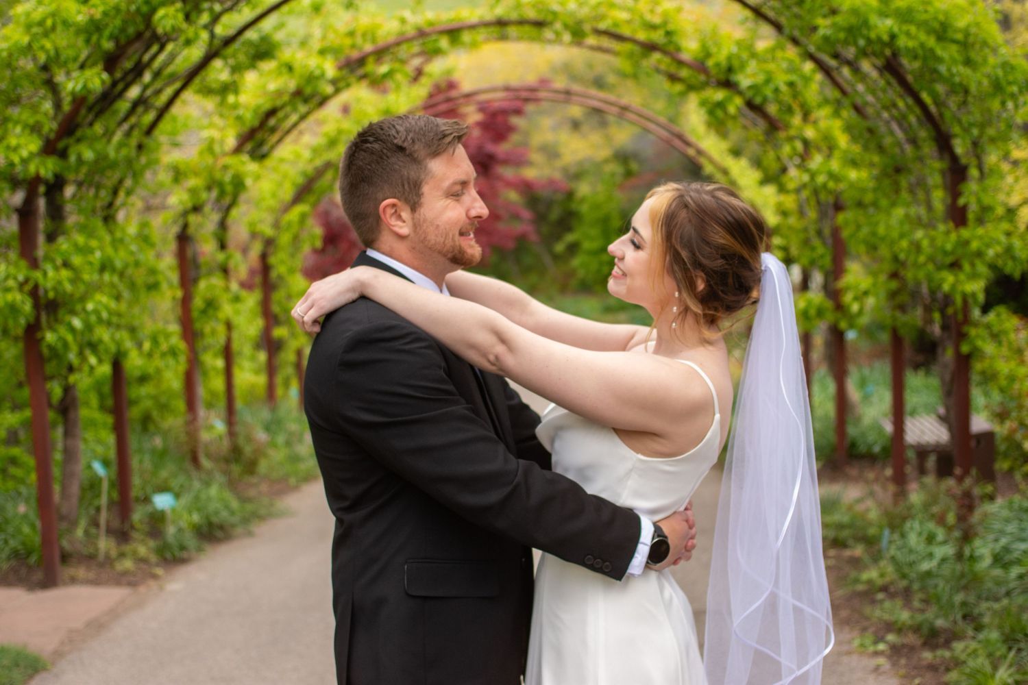Newlywed couple embraces while dancing outdoors in a lush green garden setting.