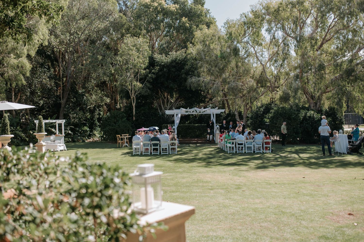 Rustic outdoor wedding venue with wooden benches and chairs arranged in a garden setting surrounded by trees.