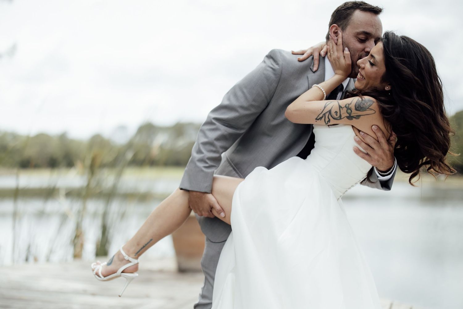 A romantic couple shares tender moments in an outdoor setting with water and nature in the background.