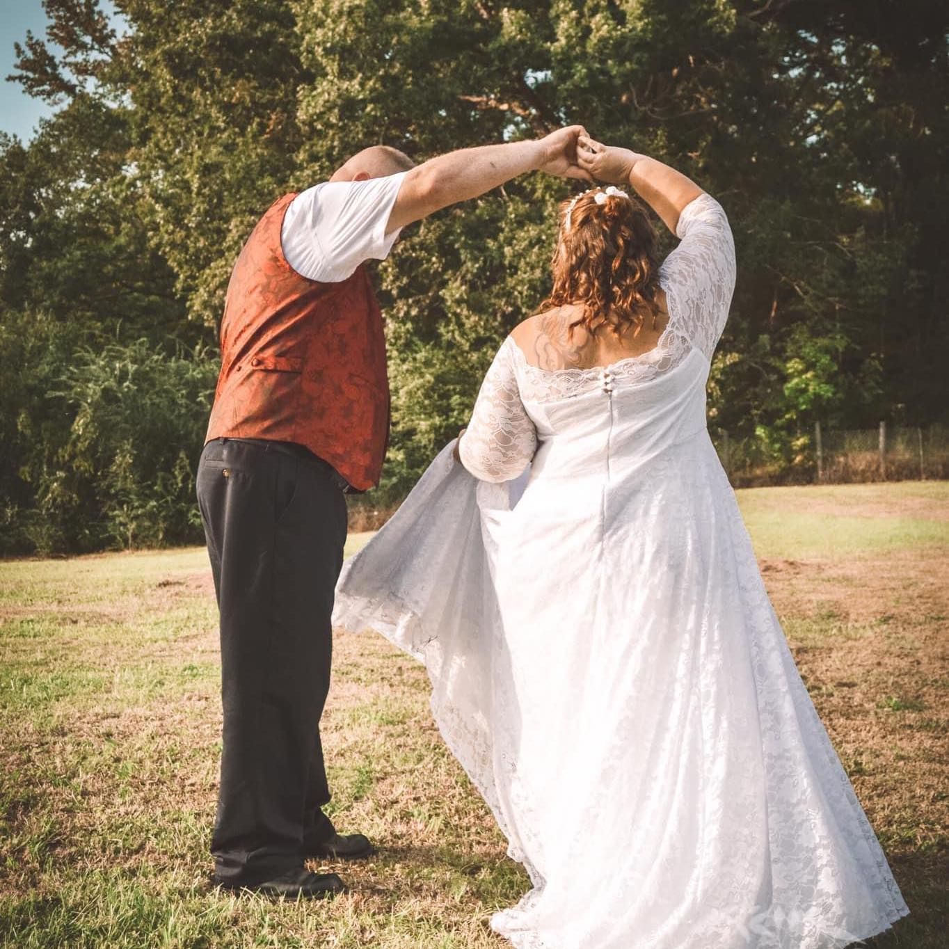 A couple dancing together in a field during a wedding celebration with trees in the background.