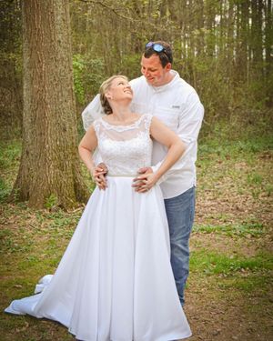 A couple dances together in a wooded area, with the bride wearing a flowing white lace dress.