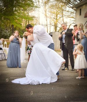 A couple shares a romantic dip kiss at their outdoor wedding celebration while guests look on and applaud.