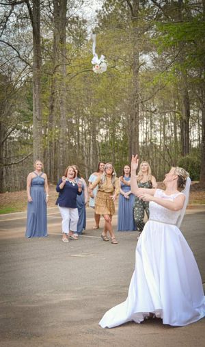 Wedding party watches as bride tosses bouquet in outdoor wooded setting.