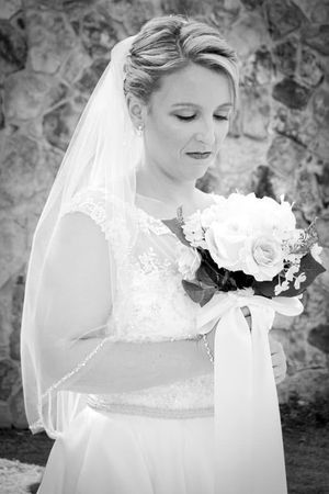 A black and white portrait of a bride holding a bouquet against a stone wall backdrop.