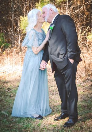 A couple in formal attire shares a romantic moment outdoors against a natural wooded backdrop.