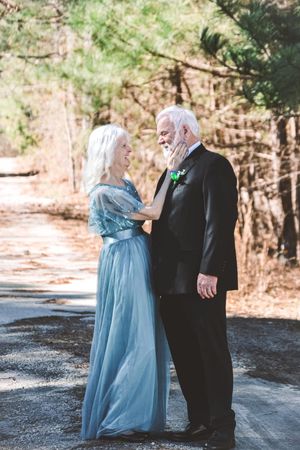 A couple in formal attire share a tender first look moment on a wooded path.