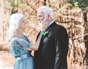 A couple in formal attire share a tender first look moment on a wooded path.
