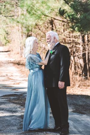 A couple in formal attire, with a light blue gown and black suit, share romantic moments on a wooded forest path.