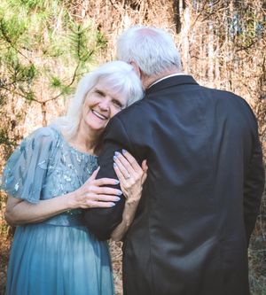 A couple in formal attire share a tender moment together in a wooded outdoor setting.