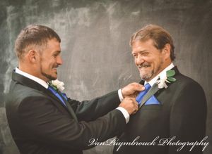 Two men in formal suits share a candid moment of laughter and joy during a wedding celebration.