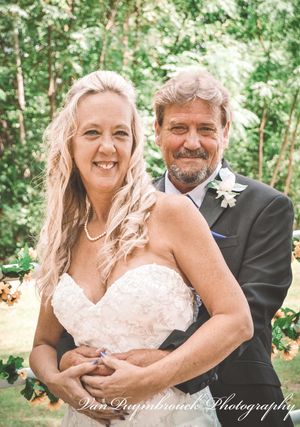 A happy couple embraces outdoors in wedding attire with a natural green forest backdrop.