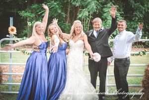 Wedding party wearing blue bridesmaid dresses poses playfully in a garden setting during summer celebration.